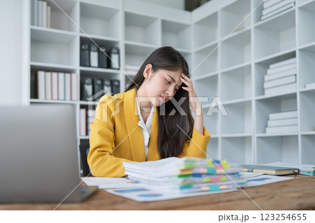 Stressed businesswoman in yellow blazer overwhelmed by paperwork and tasks in modern office environment 123254655