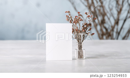 Blank card beside dried flowers in glass vase on table 123254933