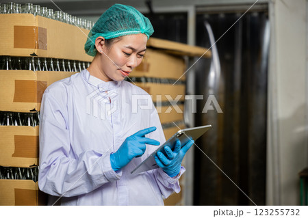 A dedicated QC woman at beverage factory uses a digital tablet to inspect items on the conveyor belt. Her role encompasses quality control while examining the bottling line for liquid manufacturing. 123255732