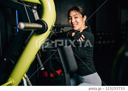 Portrait of beautiful Asian young woman performing squats on a gym machine, female working out with rowing machine at crossfit fitness, healthy lifestyle concept 123255733