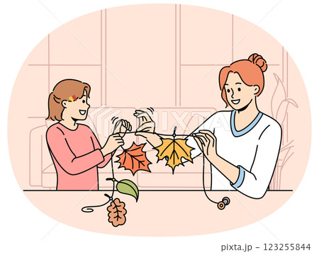 Mom and daughter make garland from tree foliage in autumn to decorate interior of house 123255844