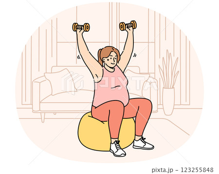 Woman doing sports, wanting to lose weight, lifts dumbbells sitting on inflatable fitness ball 123255848
