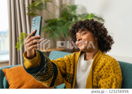 African American girl holding smartphone having video chat. Female blogger chatting with best friends in social network. Young woman having virtual meeting online chat video call at home African American girl holding smartphone having video chat. Female blogger chatting with best friends in social network. Young woman having virtual meeting online chat video call at home 123256956