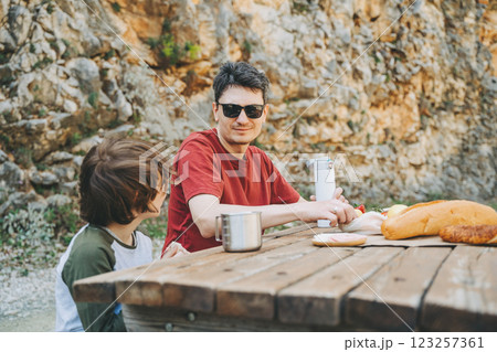 Close-up view of father and his school boy son on a family picnic in the mountains. Child kid and his dad taking a rest and enjoying a picnic while hiking in the mountains 123257361