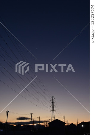 夕暮れ時の山の向こうに見える送電線と鉄塔 123257574