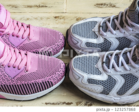 A pair of pink women's sneakers and a pair of white men's sneakers on a wooden surface 123257868