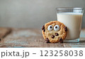 A playful chocolate chip cookie with googly eyes sits beside a glass of milk 123258038