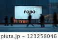 A large advertising screen displays the word 'FOBO' prominently. Silhouetted pedestrians walk by in a modern urban setting. The background features buildings and a subtle glow. 123258046