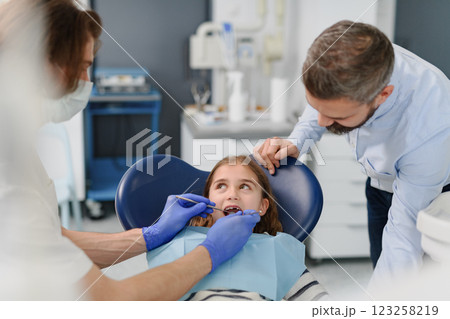 Cute girl during annual dental check-up in dental clinic, father supporting her. 123258219