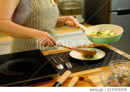Cropped shot woman serving freshly cooked dish onto a plate in a kitchen 123259309