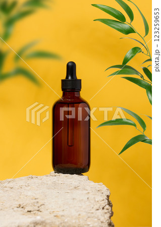 Transparent brown glass bottle with black pipette stands on stone, yellow background. Cosmetics and oils Transparent brown glass bottle with black pipette stands on stone, yellow background. Cosmetics and oils 123259653