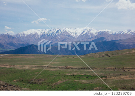 A beautiful landscape of snow-capped mountains and green meadows and a sky with clouds A beautiful landscape of snow-capped mountains and green meadows and a sky with clouds 123259709