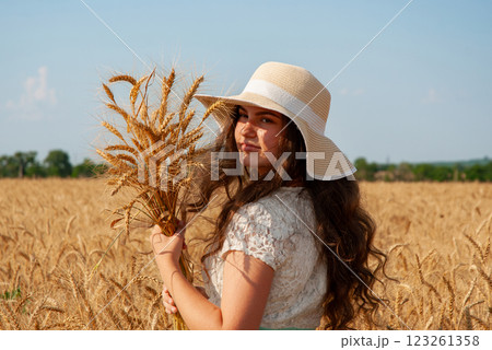 Woman in summer hat holding wheat in a sunny field. Harvesting concept Woman in summer hat holding wheat in a sunny field. Harvesting concept 123261358