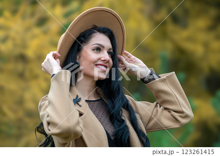 Beautiful brunette girl in beige coat and hat posing in autumn park 123261415