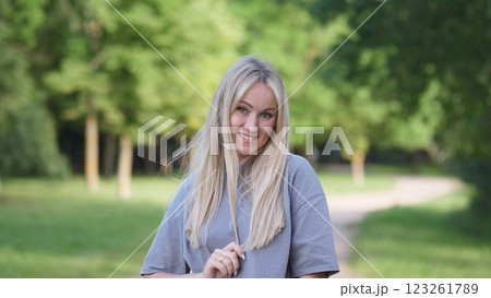 A cheerful young woman with flowing blonde hair is joyfully enjoying a beautiful sunny day in a lovely green park 123261789