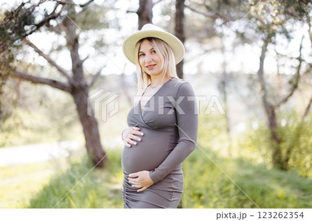 Beautiful pregnant woman in hat and dress walking in the forest. Woman expecting baby born. Beautiful pregnant woman in hat and dress walking in the forest. Woman expecting baby born. 123262354