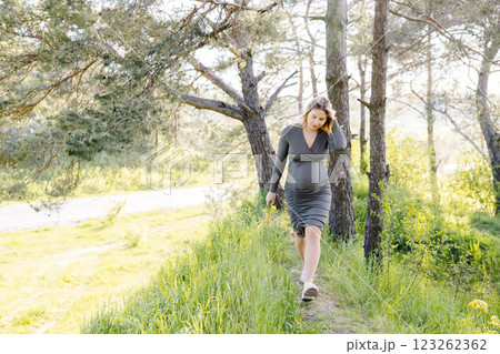 Beautiful pregnant woman in hat and dress walking in the forest. Woman expecting baby born. 123262362