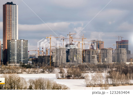 Urban development in a bustling city with skyscrapers and craned constructions near a frozen lake during winter Urban development in a bustling city with skyscrapers and craned constructions near a frozen lake during winter 123263404