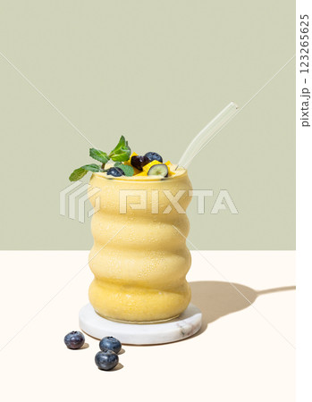 Smoothie with mango, banana and blueberry in a glass on a yellow and green background 123265625