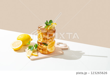 Iced tea with lemon, ice and mint in a glass on wooden board on a white and beige background Iced tea with lemon, ice and mint in a glass on wooden board on a white and beige background 123265626
