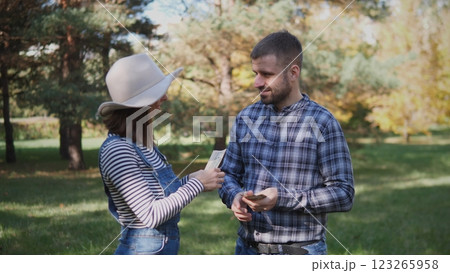 Two young adults are joyfully interacting outdoors, exchanging various items amidst a vibrant natural setting 123265958