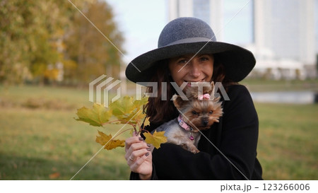 A joyful woman warmly embraces her small dog while surrounded by colorful autumn leaves in a serene park setting 123266006