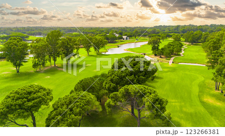 Panoramic view of a golf course with a winding river, lush greenery, and a cloudy sky Panoramic view of a golf course with a winding river, lush greenery, and a cloudy sky 123266381