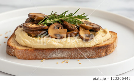Whole grain toast topped with hummus, sauteed mushrooms, rosemary, egg white foam, sesame seeds, and tahini sauce on a sleek marble surface. Soft lighting enhances textures. 123266443