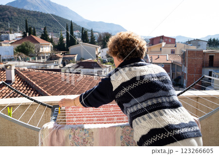 Woman hanging laundry on a terrace with tiled roofs and mountain view. 123266605