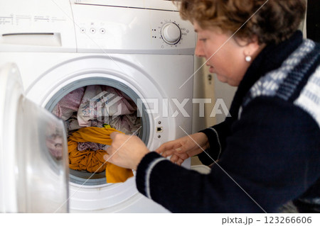 Mature woman taking clean laundry from washing machine, household chores. 123266606