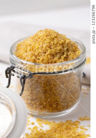 Opened glass jar of raw dry uncooked yellow bulgur grain on white table cloesup. Ancient food Opened glass jar of raw dry uncooked yellow bulgur grain on white table cloesup. Ancient food 123266796