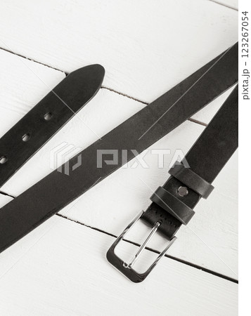 Black leather belt on a white wooden background. Black leather belt on a white wooden background. 123267054