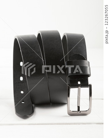 Black genuine leather belt on a white wooden background. Black genuine leather belt on a white wooden background. 123267055