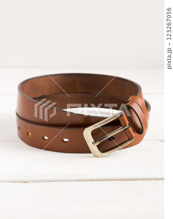 Brown genuine leather belt on a white wooden background. Brown genuine leather belt on a white wooden background. 123267056