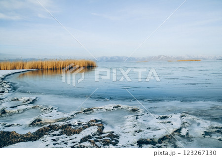 Frozen lake and snowy mountains. Tall grasses on the lake. Bamboo and frozen river. Beautiful winter landscape with lake and mountains. Ice lake	 Frozen lake and snowy mountains. Tall grasses on the lake. Bamboo and frozen river. Beautiful winter landscape with lake and mountains. Ice lake	 123267130