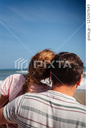 Father and daughter stand on the beach, gazing at the waves, sharing a moment of reflection by the 123267643