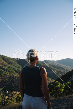 A woman stands on a mountain overlook, gazing at the expansive landscape under a clear blue sky A woman stands on a mountain overlook, gazing at the expansive landscape under a clear blue sky 123267666