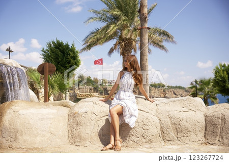 Woman in summer dress sitting by waterfall and palm trees in Park of Antalya Woman in summer dress sitting by waterfall and palm trees in Park of Antalya 123267724