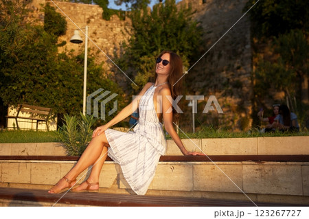 Smiling woman relaxing on bench at sunset  123267727