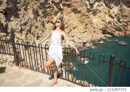 Joyful woman in summer dress embracing ocean breeze on cliffs Joyful woman in summer dress embracing ocean breeze on cliffs 123267731