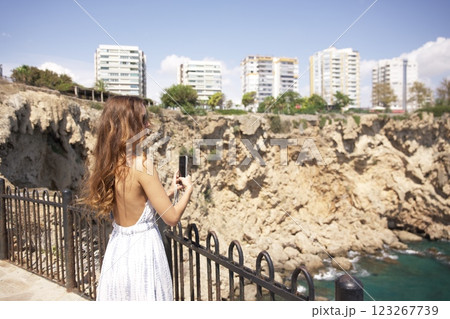 Woman in summer dress taking photo of coastal cliffs  123267739