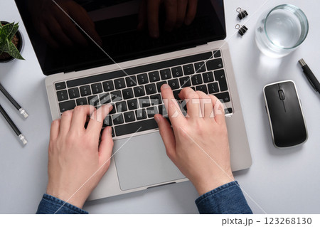 Men's hands typing on a laptop keyboard. Desktop with a plant, stationery, mouse, glass of water. Men's hands typing on a laptop keyboard. Desktop with a plant, stationery, mouse, glass of water. 123268130