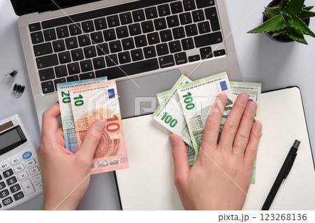 Hands counting euro banknotes over a notebook and notepad on an office desk. Idea passive income, remote work, digital business 123268136