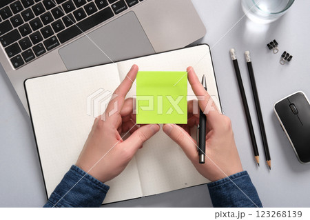 Hands holding a blank sticky note in green over an open notepad on a table. A place for your text Hands holding a blank sticky note in green over an open notepad on a table. A place for your text 123268139
