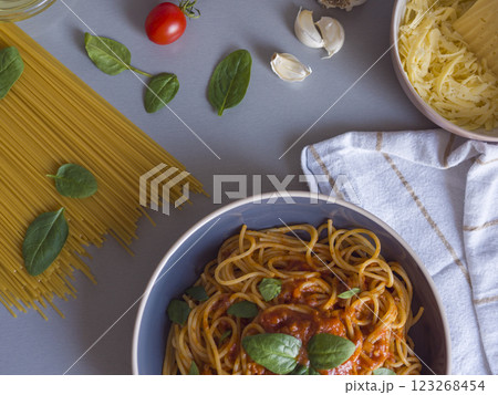 Balanesi pasta drizzled with tomato sauce, garnished with basil, nestled among raw spaghetti, cherry tomatoes, garlic, cheese, and spinach on gray surface Balanesi pasta drizzled with tomato sauce, garnished with basil, nestled among raw spaghetti, cherry tomatoes, garlic, cheese, and spinach on gray surface 123268454