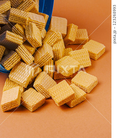 Sweet wafers spilled out of a blue container on orange surface 123268993