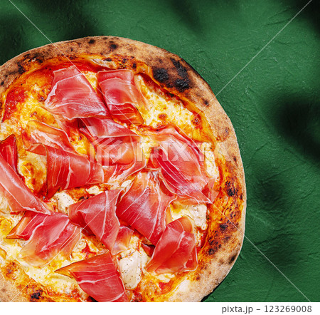 Savory pizza topped with prosciutto and fresh cheese on green table Savory pizza topped with prosciutto and fresh cheese on green table 123269008