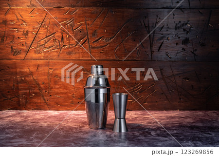 Iron shaker and measuring glass. Shaker and bartender's glass. Cocktail making set. Dishes on a wooden background. Ray of light on the background. 123269856