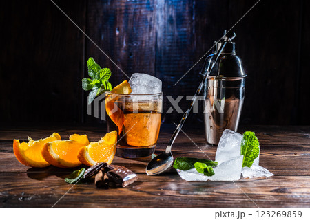 A glass of whiskey and a large ice cube. Steel shaker and bartender's spoon. Sliced citrus and mint. 123269859
