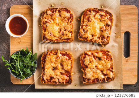 Close up of baked sandwiches with bacon, cheese and tomato sauce on a board on a table top view 123270695